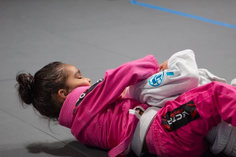 A young girl in a pink gi clinching with a partner