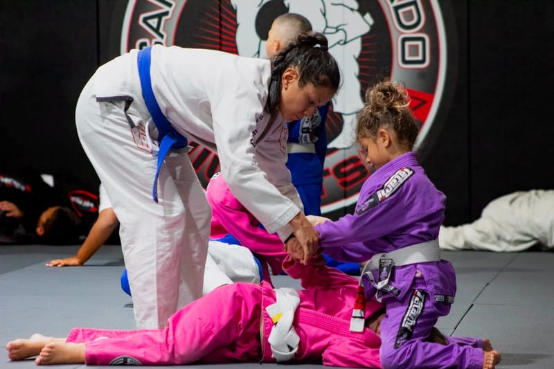 A female coach guiding young girls on the mat